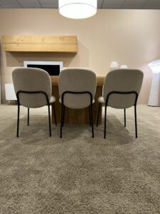 Tres sillas tapizadas en beige frente a una mesa de madera en una sala con alfombra beige y lámparas modernas