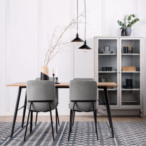 Comedor minimalista con mesa de madera, dos sillas grises, lámparas colgantes negras y vitrina con vajilla y decoración
